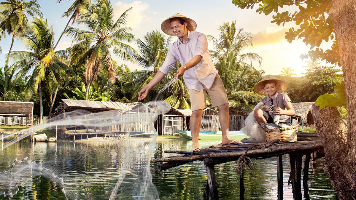 Một anh, có con trai bên cạnh, đang thả lưới đánh cá trên một bến đò.