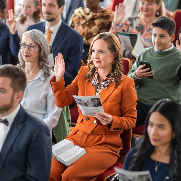 Una hermana levanta la mano durante el Estudio de “La Atalaya”. Otros hermanos y hermanas también levantan la mano.