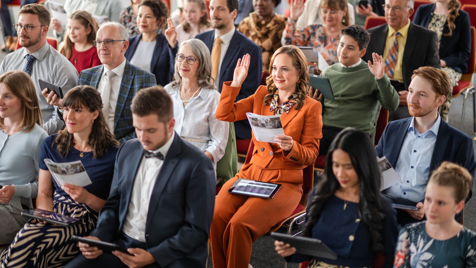 Una hermana levanta la mano durante el Estudio de “La Atalaya”. Otros hermanos y hermanas también levantan la mano.