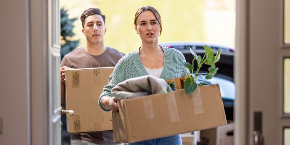 One man and one woman carry carton wey their things dey de enter house.