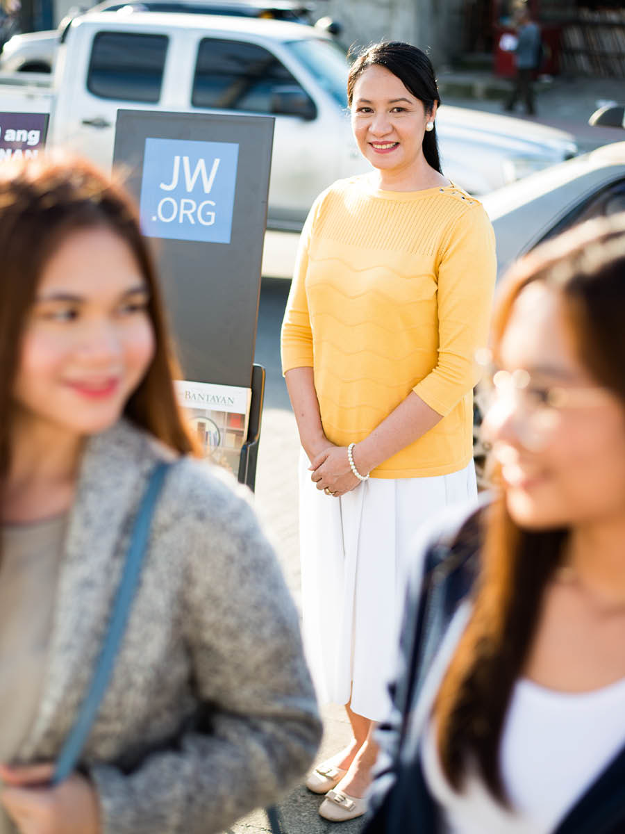 Helen stand near magazine-stand and e de smile. Two women de waka pass-am.