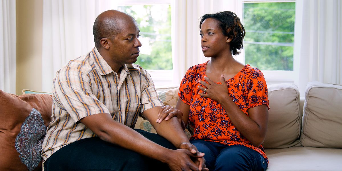Tọkọtaya kan jókòó ti ara wọn, ọkọ tẹ́tí sílẹ̀ bí ìyàwó rẹ ṣe ń sọ ẹ̀dùn ọkàn rẹ̀ fún un