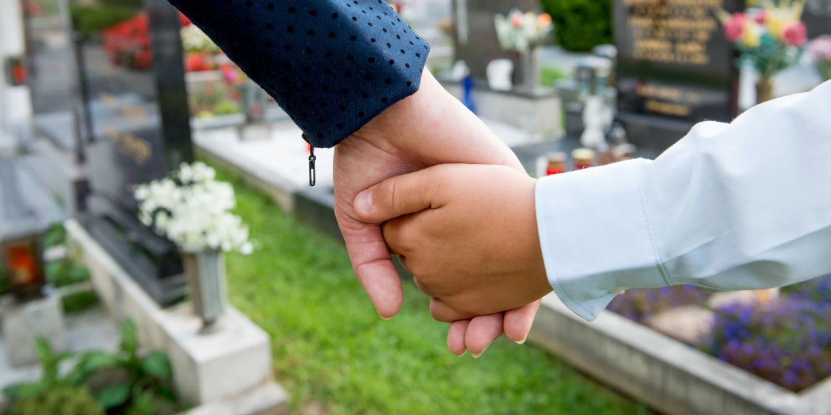 Ọmọdé kan di ọwọ́ àgbàlagbà kan mú ní itẹ́ òkú