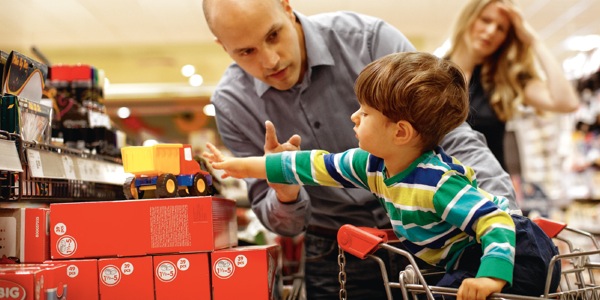 一个小孩伸手拿货架上的玩具时，他的爸爸说不可以