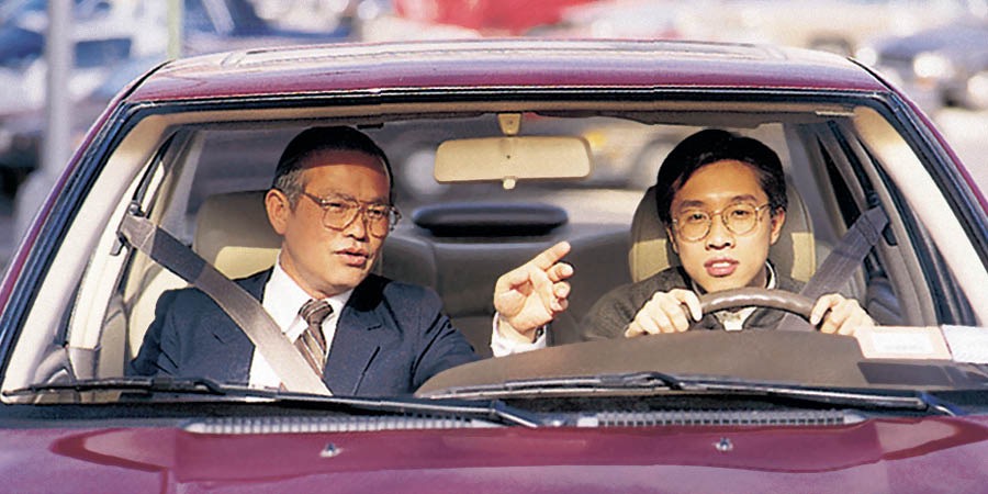 一个男子喺度揸车，旁边有人指导紧佢