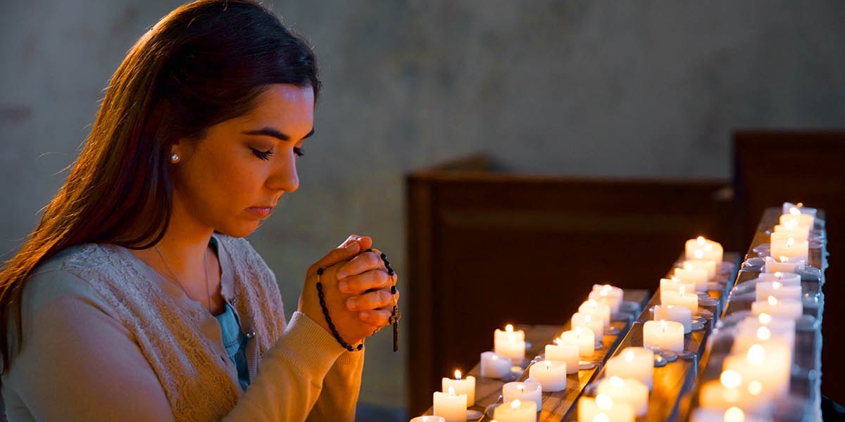 女子在燃着的蜡烛前祷告，手里拿着念珠
