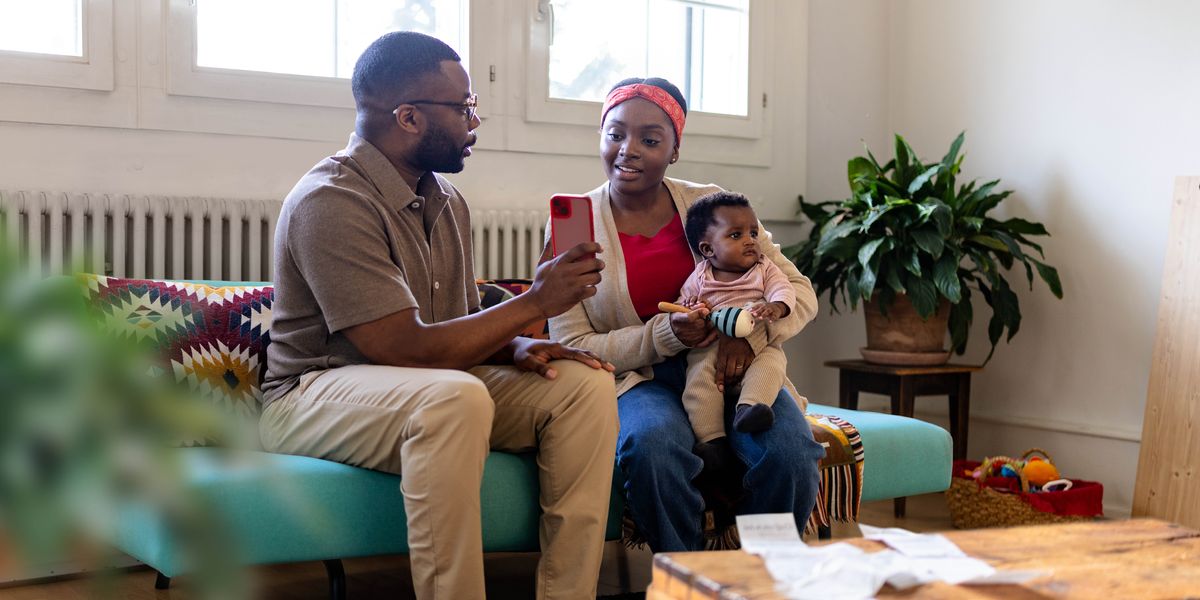 A husband showing his wife something on a smartphone while she holds their young son.