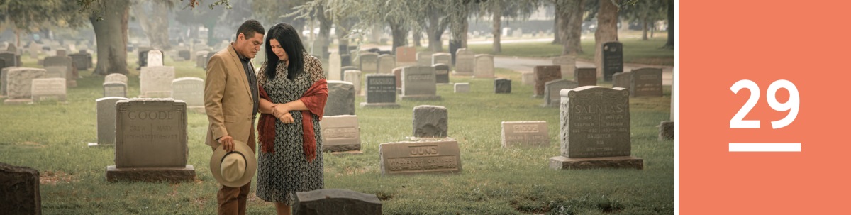 Lesson 29. A couple prays in front of a headstone in a cemetery.