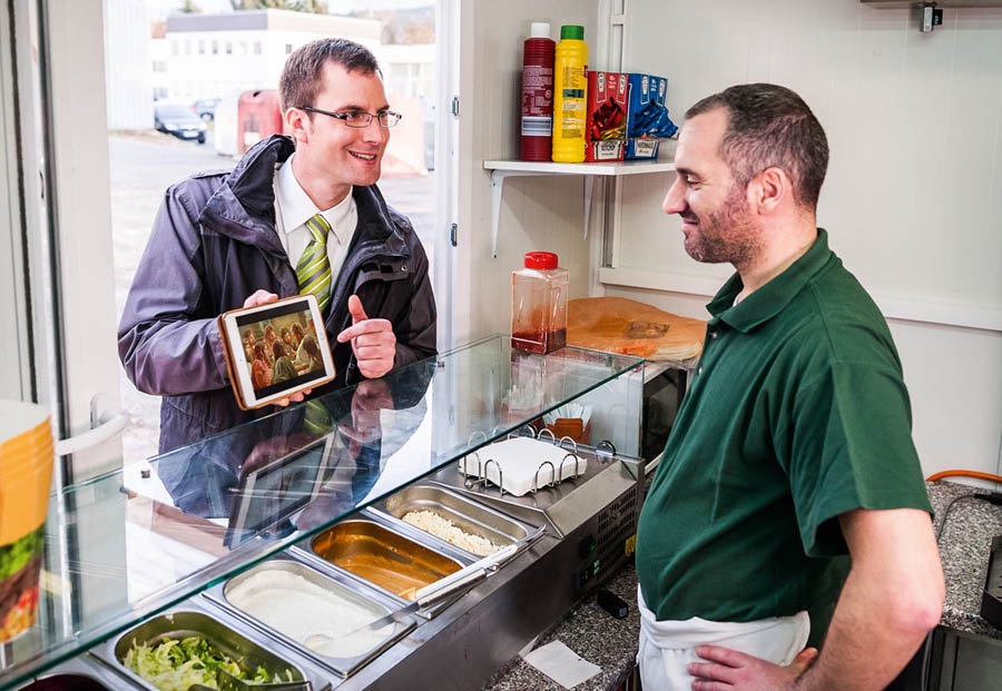 Collage: 1. A brother witnessing to a man while on a break at work. 2. A brother showing a video to a restaurant worker.