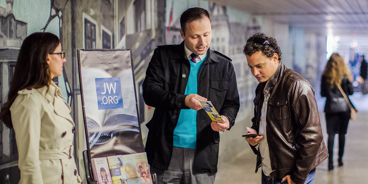 A Witness couple offering a tract to a man while doing cart witnessing in a subway station.