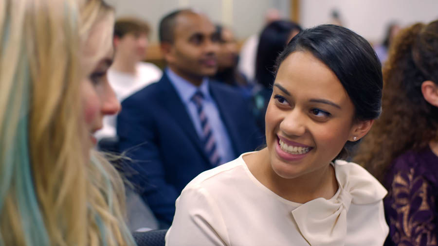 A scene from the video “Help Your Bible Students to Attend Meetings.” Neeta smiles as Jade sits next to her during a congregation meeting.