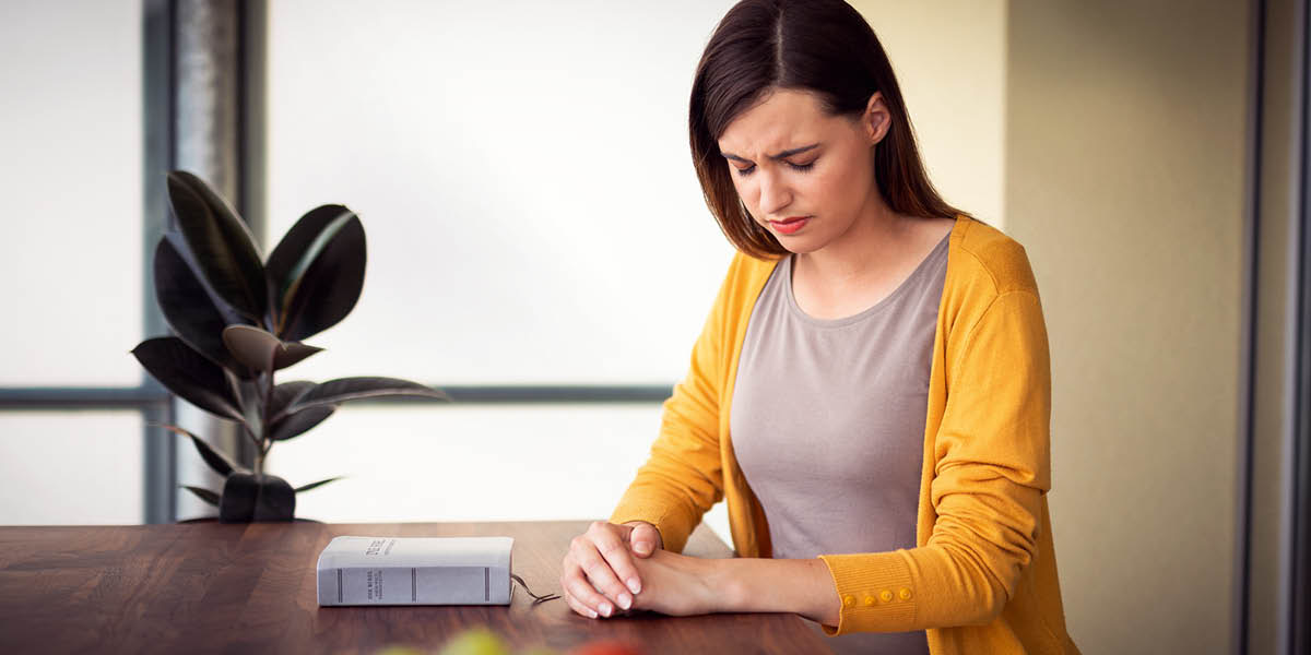 A sister praying. Her Bible sits on the table in front of her.