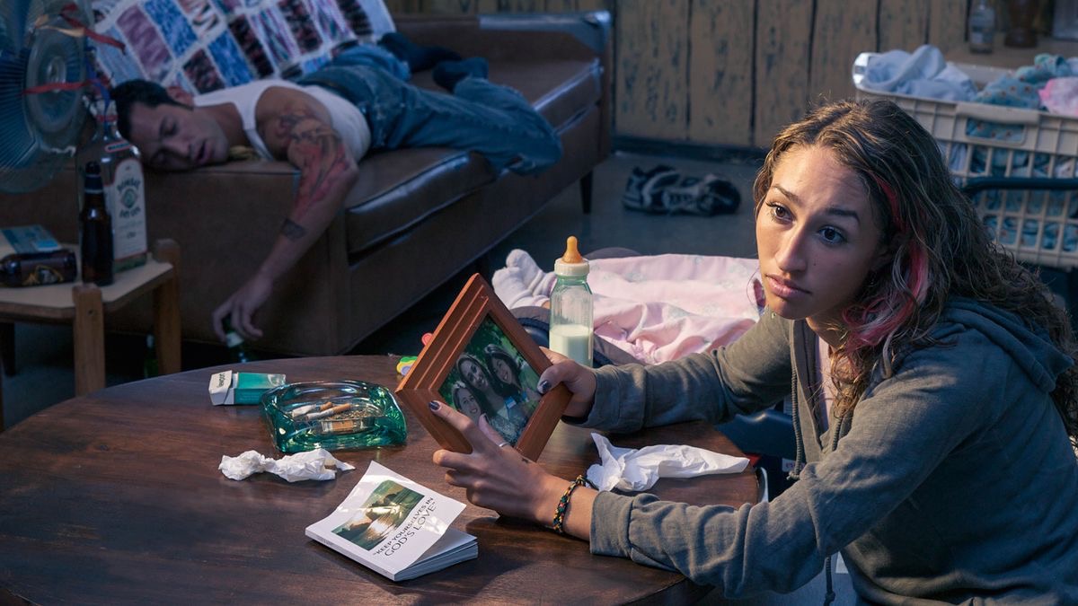 A sister who married a non-Witness, now with a baby, reflecting longingly on her life when she was more active spiritually. On the table in front of her is an ashtray with cigarette butts. Her drunk husband is sleeping on a sofa.